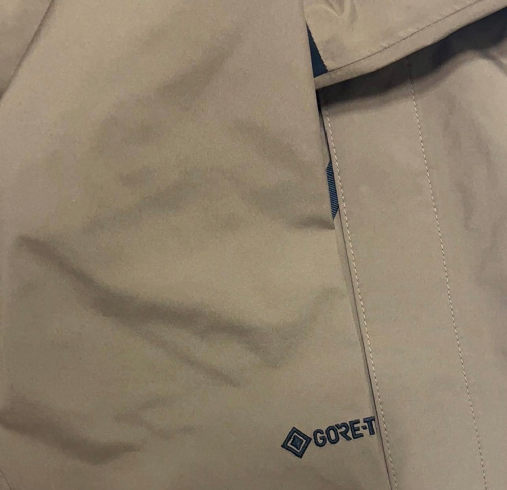 Tan jacket fabric with GORE‑TEX logo patch near a stitched seam