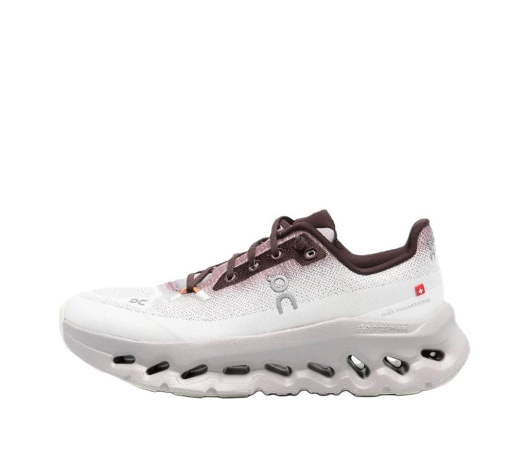 Sneaker in white with brown trim, lace-up front, and rocker-style sole cutouts