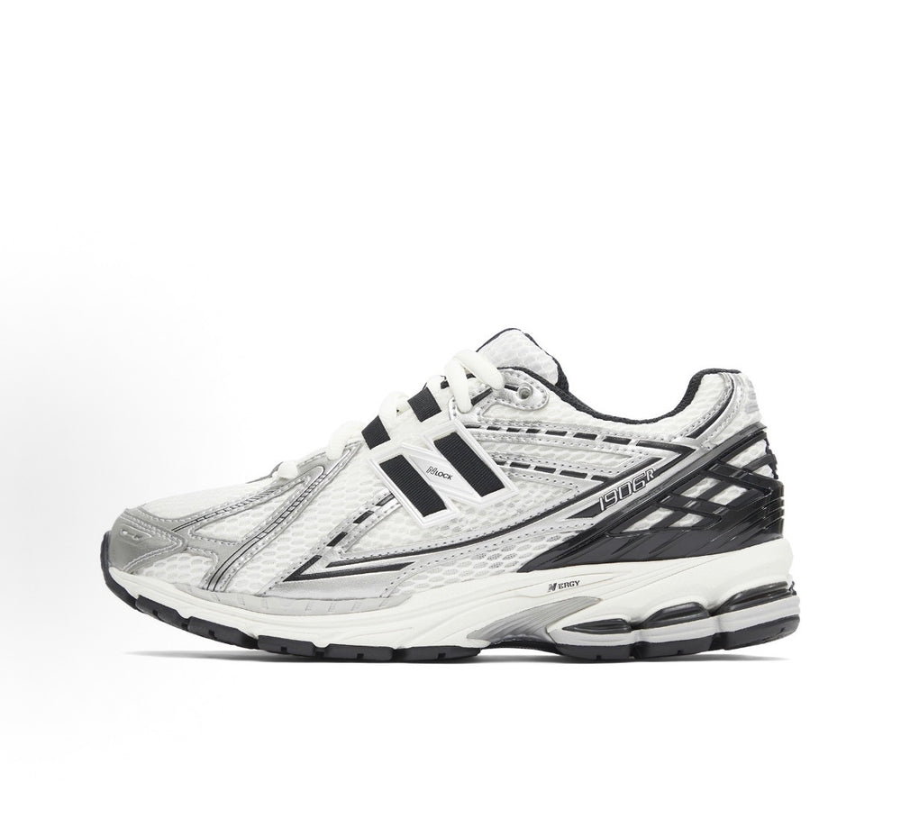 New Balance 1906R side profile sneaker in silver with black stripes and thick midsole.