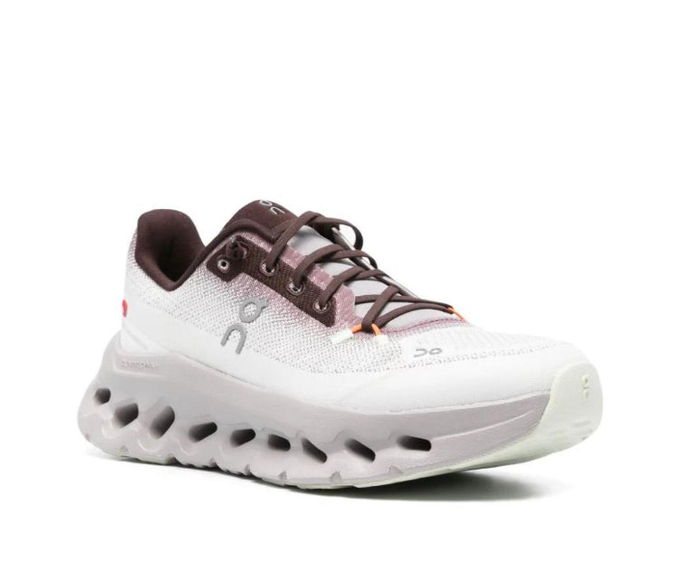 Sneaker with white textured upper, brown lace eyelets, and thick grippy sole